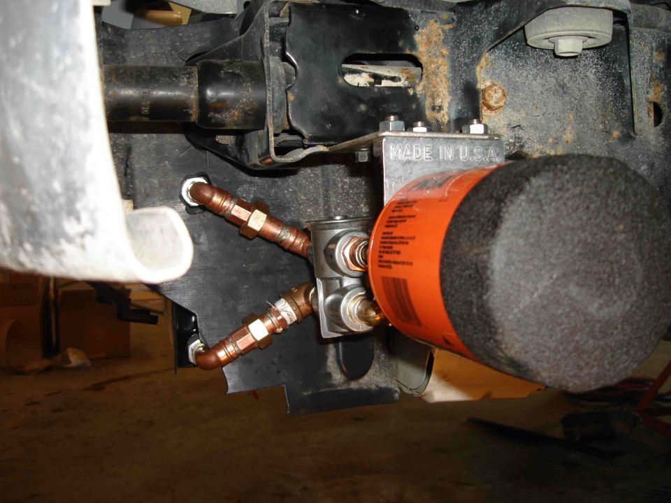 Remote oil filter mount under white car with orange filter and copper oil lines