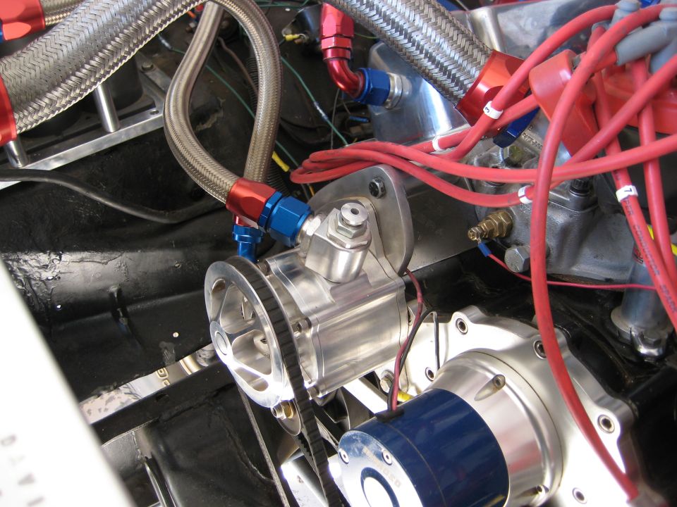 Close-up of engine parts including braided hoses, pulleys, and red spark plug wires
