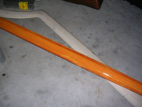 1975 Ford Ranchero - A wooden trim piece with an orange stain sits on a concrete floor next to another piece of wood.