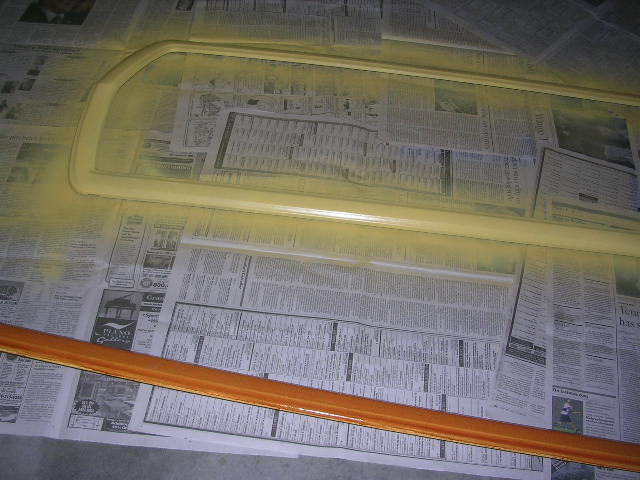 Yellow painted car window trim and a wooden trim piece on newspaper