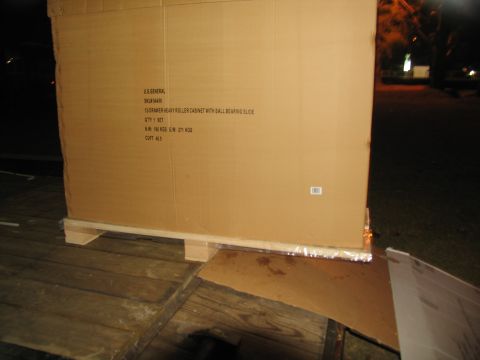 1988 Ford C-350 (Centurion Conversions) - A large cardboard box containing a roller cabinet sits on a wooden pallet outdoors at night.
