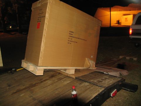 1988 Ford C-350 (Centurion Conversions) - A large cardboard box is loaded onto a trailer, with a white truck visible in the background at night.