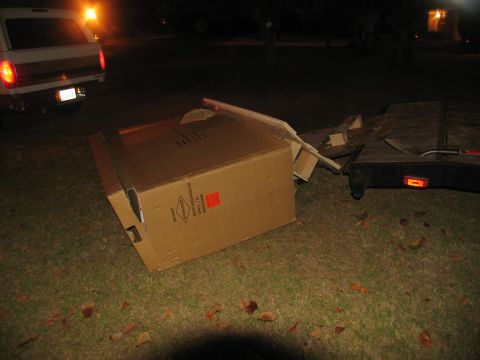 1988 Ford C-350 (Centurion Conversions) - A large cardboard box has fallen out of a trailer, with a van parked close by at night.
