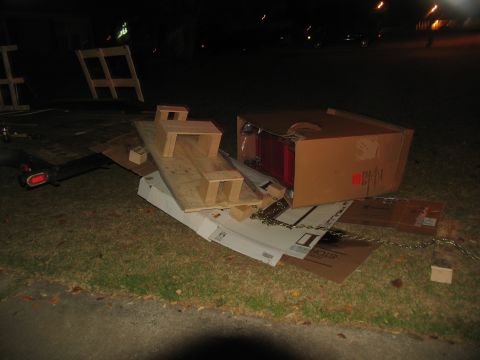 1988 Ford C-350 (Centurion Conversions) - A collection of building materials and a trailer are piled on the grass at night.