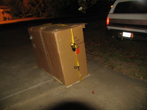 1988 Ford C-350 (Centurion Conversions) - A large, secured cardboard box is being towed by a pickup truck on a paved surface at night.