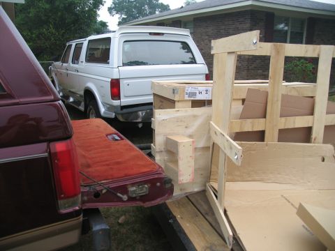 1988 Ford C-350 (Centurion Conversions) - White Ford Bronco with a cap is parked next to a trailer loaded with wooden crates and boxes.