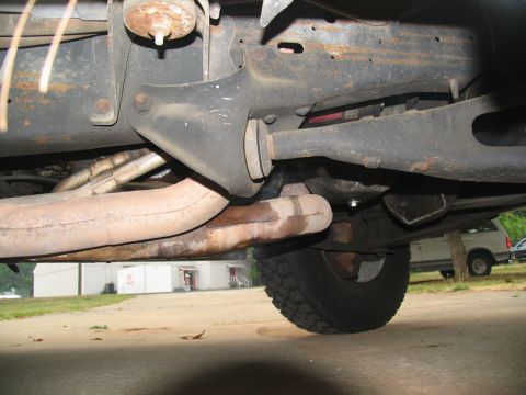 1988 Ford C-350 (Centurion Conversions) - The photo shows the undercarriage of a vehicle, including the frame, exhaust system, and a tire. A second vehicle is parked in the backgrou…