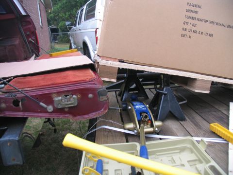 1988 Ford C-350 (Centurion Conversions) - A silver van is parked next to a red vehicle's open tailgate, with a large box on jack stands.