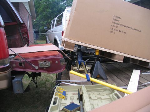 1988 Ford C-350 (Centurion Conversions) - A silver van and a red truck tailgate are visible as a large cardboard box is being unloaded from a trailer.
