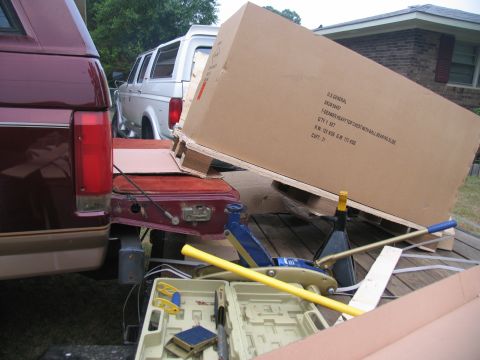 1988 Ford C-350 (Centurion Conversions) - A maroon pickup truck and a white van are parked next to a trailer carrying a large cardboard box.