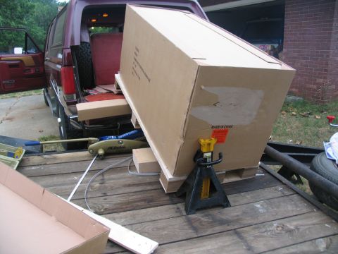 1988 Ford C-350 (Centurion Conversions) - A large box is being loaded from a trailer into the back of a red SUV using a jack and jack stands.
