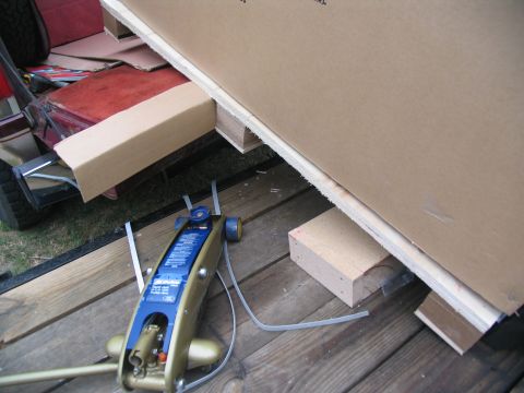 1988 Ford C-350 (Centurion Conversions) - A blue hydraulic jack rests on a wooden trailer bed next to large cardboard sheets being secured with wooden blocks.
