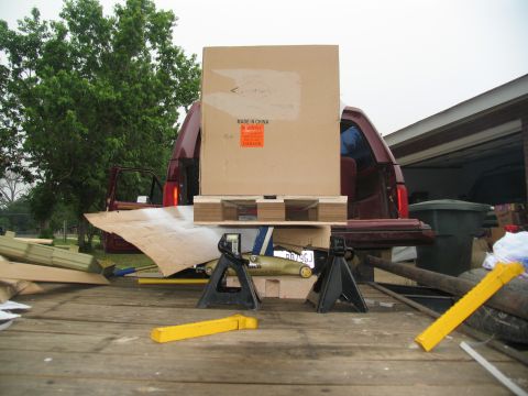 1988 Ford C-350 (Centurion Conversions) - A red pickup truck bed is filled with various items, including a large box supported by jack stands.