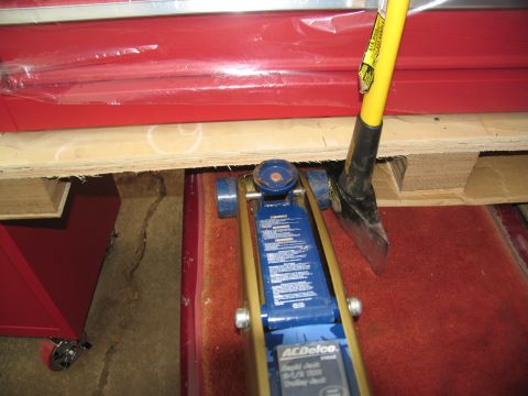 1988 Ford C-350 (Centurion Conversions) - A blue hydraulic jack and a shovel are positioned on a red carpet beneath a wooden pallet.