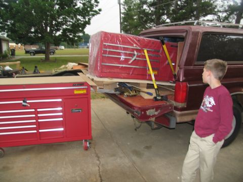 1988 Ford C-350 (Centurion Conversions) - A large red toolbox, wrapped in plastic, is being loaded onto a pickup truck, with another red toolbox nearby.