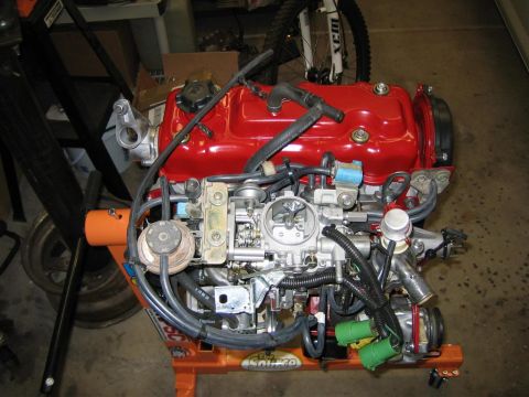 1987 Suzuki Samurai - Engine assembly displayed on an orange stand, a red valve cover and visible carburetor components.
