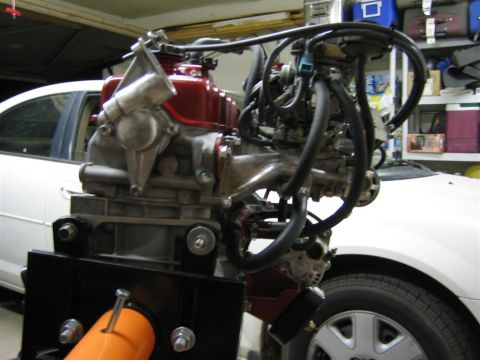 1987 Suzuki Samurai - Engine assembly with various hoses and components, partially obscuring a white vehicle.