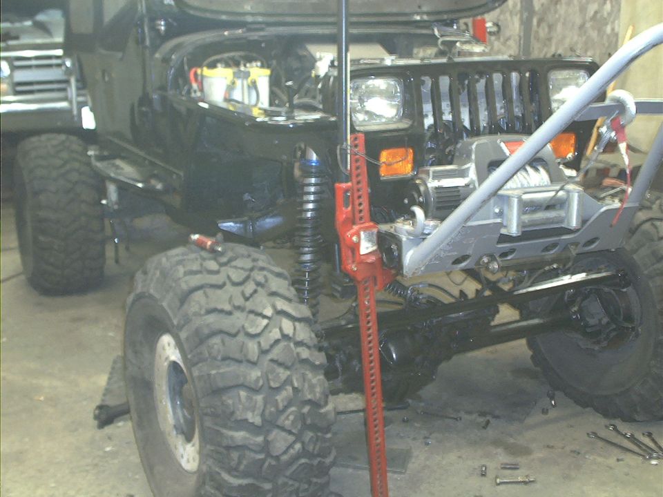 Front view of black Jeep with large off-road tires, winch, and Hi-Lift jack