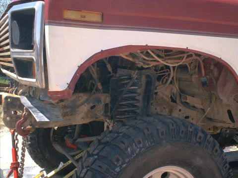1986 Ford Bronco - Close-up of the front section of a red and white truck, showing its suspension and tire.