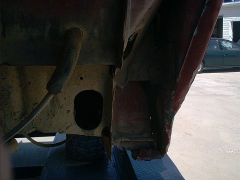 1986 Ford Bronco - Close-up view of a heavily rusted vehicle frame section with a hose, indicating significant wear.