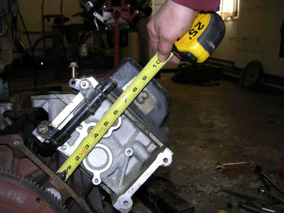 Hand measuring aluminum transmission case face with tape measure in workshop