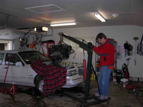 1997 Lincoln Town Car - An engine is being lifted out of a white Lincoln Town Car with an engine hoist in a garage setting.