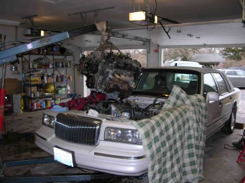 1997 Lincoln Town Car - Engine removal in progress on a white Lincoln Town Car inside a garage.