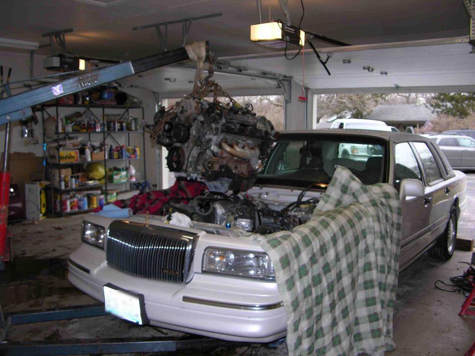White Lincoln Town Car in garage with engine hoisted out of the bay during engine work