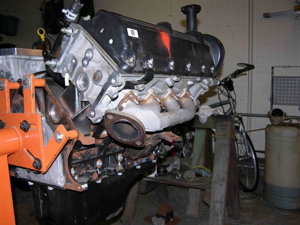 V8 engine on orange stand in garage with exhaust manifold and black oil pan