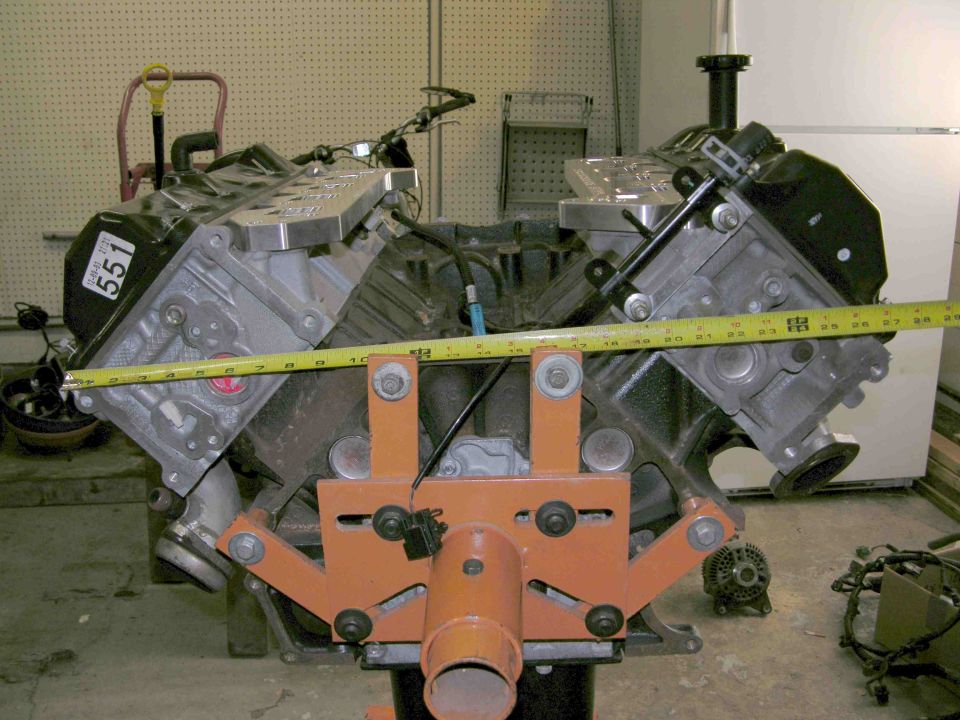 V8 engine block on stand with tape measure across cylinder heads, marked 5.51