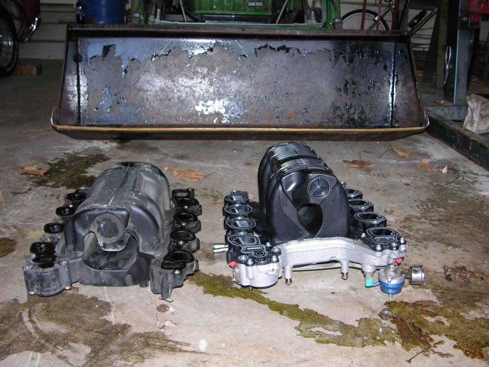 Two intake manifolds on a concrete floor, one black plastic, one silver and black