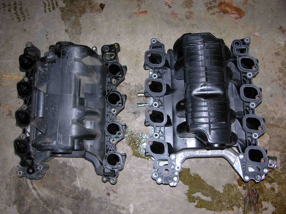 Two black plastic intake manifolds on a concrete floor. One has a Ford logo and part number visible