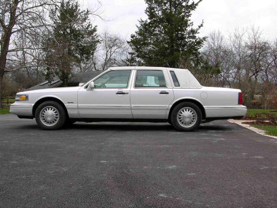 White Lincoln Town Car sedan, driver-side profile on asphalt driveway
