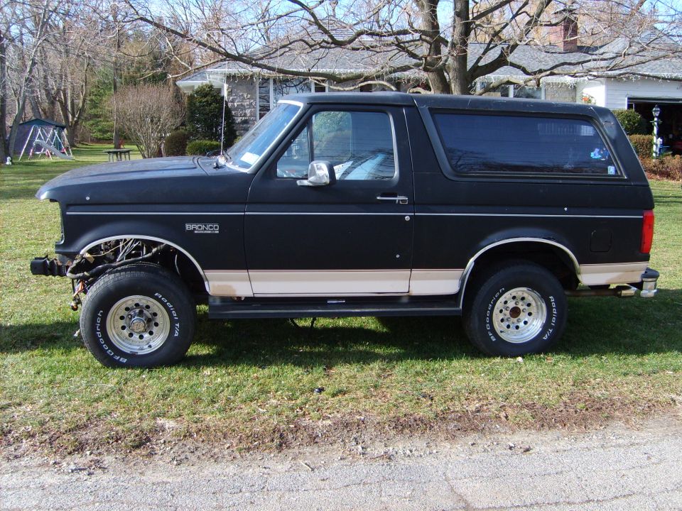 Black lifted Ford Bronco SUV side view on grass, missing front bumper, chrome wheels with BFGoodrich tires