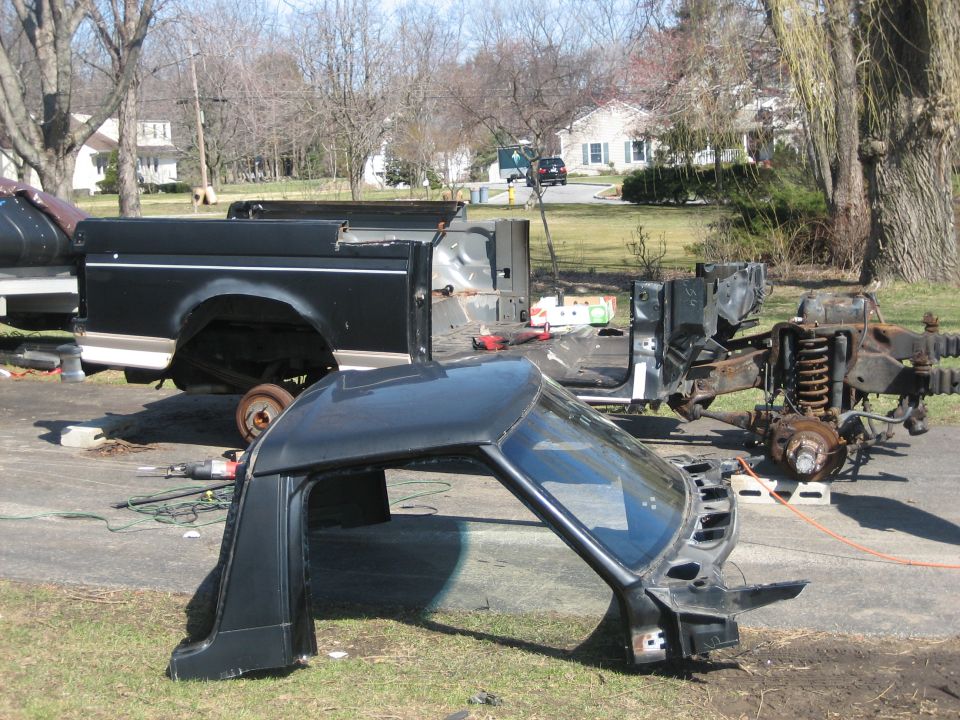 Disassembled pickup truck parts including bed, frame and body on a driveway