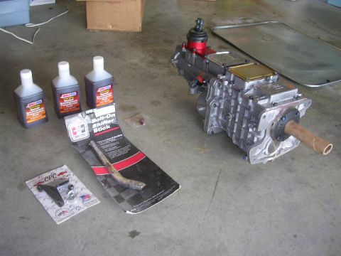 1975 Ford Ranchero - A transmission and parts are laid out on a concrete floor, likely for installation or repair.