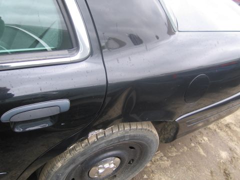 1991 Ford LTD Crown Victoria - A black sedan's rear side shows damage, including a dent and rust around the tire.