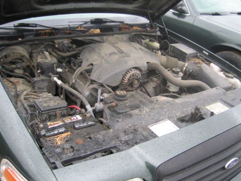 1991 Ford LTD Crown Victoria - The engine bay of a Ford Crown Victoria is shown with the hood open, revealing the engine and battery. Another vehicle is visible to the ri…