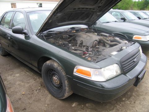 1991 Ford LTD Crown Victoria - A dark green sedan with its hood open reveals the engine bay, parked outdoors with other vehicles in the background.