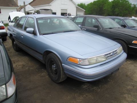 1991 Ford LTD Crown Victoria - A light blue sedan is parked in a lot with other vehicles, some with hoods open.