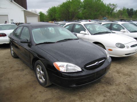 1991 Ford LTD Crown Victoria - A black Ford Taurus is parked in a lot with other vehicles, including a white Ford Taurus.