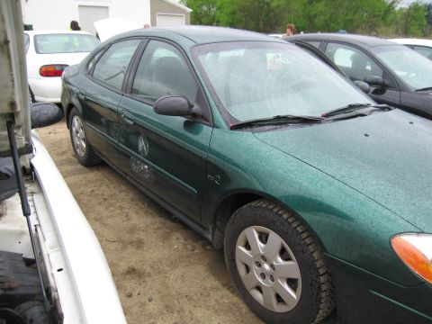 1991 Ford LTD Crown Victoria - A green sedan is parked outdoors next to other vehicles, with raindrops on its surface.