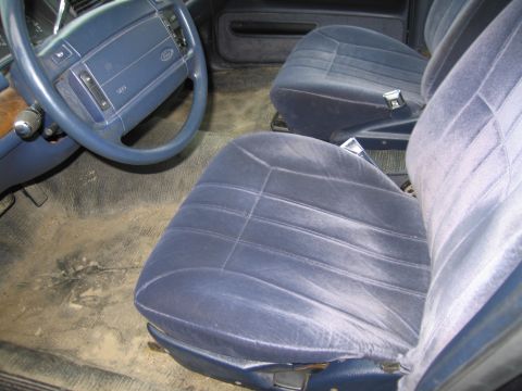 1991 Ford LTD Crown Victoria - The interior of a car shows blue velour seats and a blue steering wheel with a dirty floor.