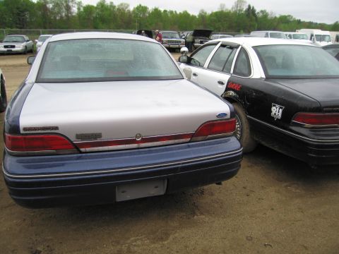 1991 Ford LTD Crown Victoria - A two-tone Ford Crown Victoria is parked next to a police car, with other vehicles in the background.