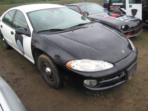 1991 Ford LTD Crown Victoria - A two-tone police car is parked on a muddy lot next to other vehicles.