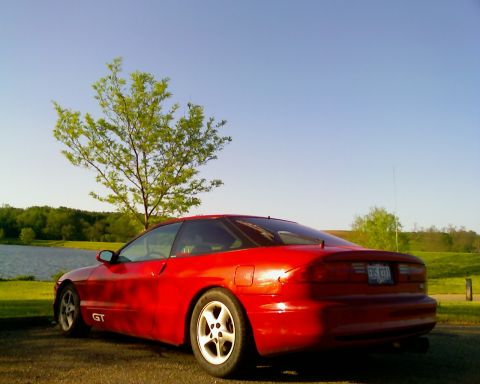 1993 Ford Probe - A red 1993 Ford Probe GT is parked near a body of water under a clear blue sky.