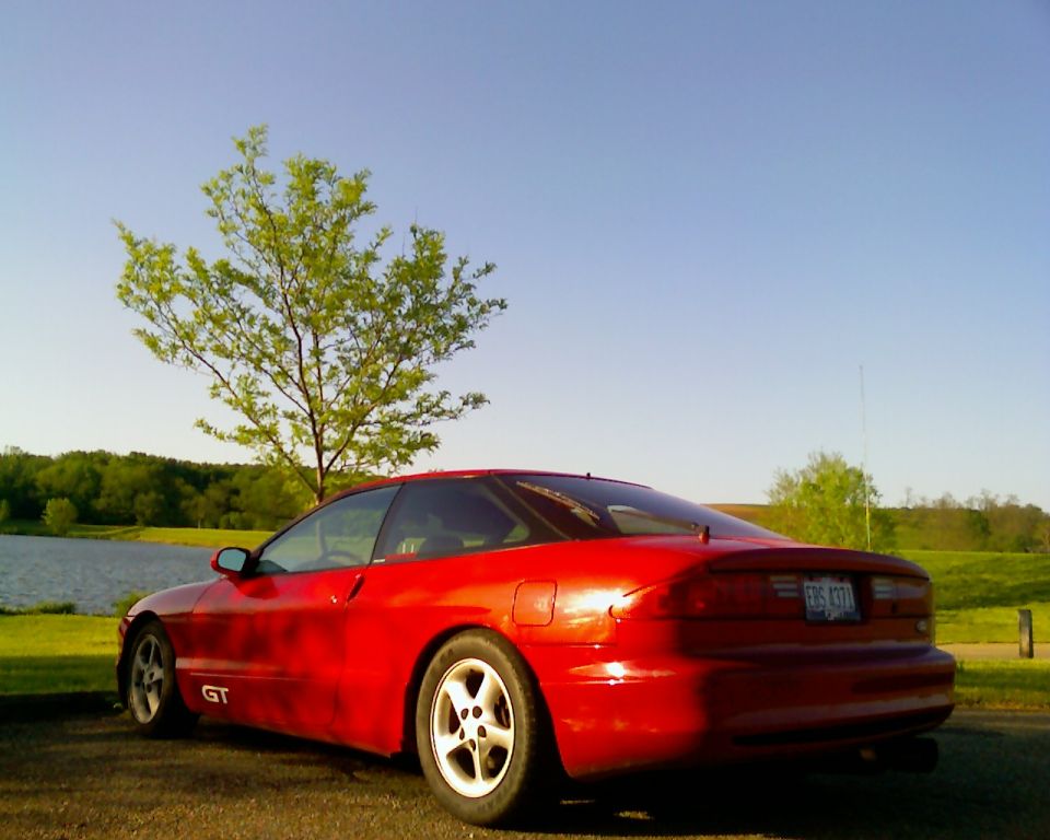 Red 1993 Ford Probe GT parked by a lake with a tree