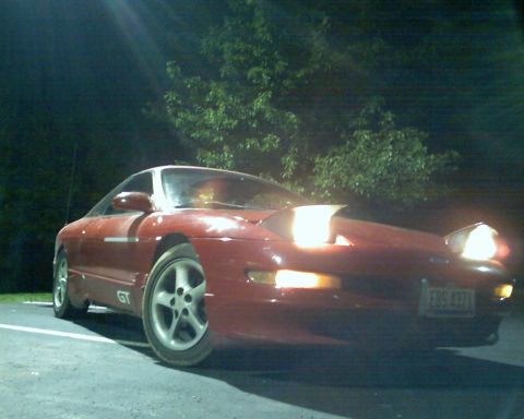 1993 Ford Probe - A red 1993 Ford Probe GT coupe is parked at night, its pop-up headlights illuminated.