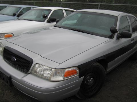 1991 Ford LTD Crown Victoria - Silver police car with black stripe, parked in a lot with other vehicles.