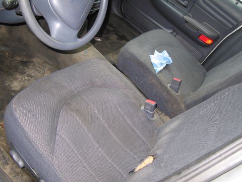 1991 Ford LTD Crown Victoria - The interior of a car shows worn fabric seats, a steering wheel, and a door panel with a red reflector.